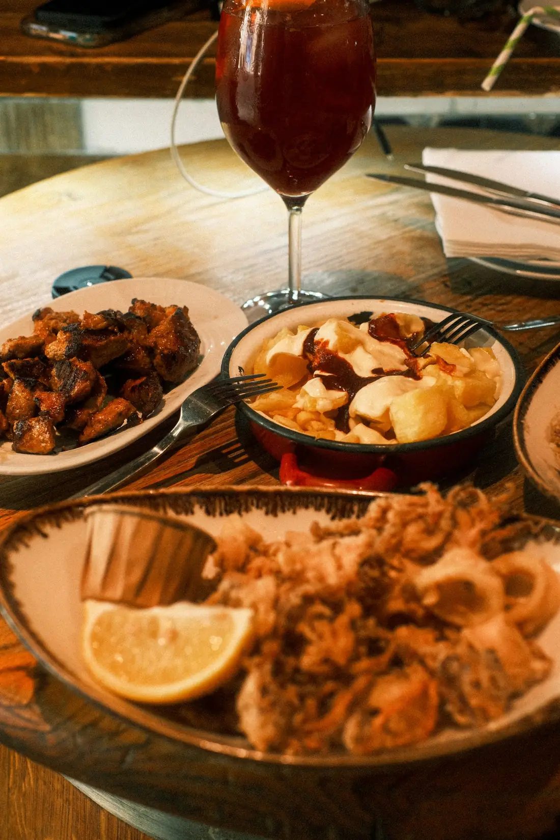 Mesa de madera con varias tapas y una copa de vino tinto